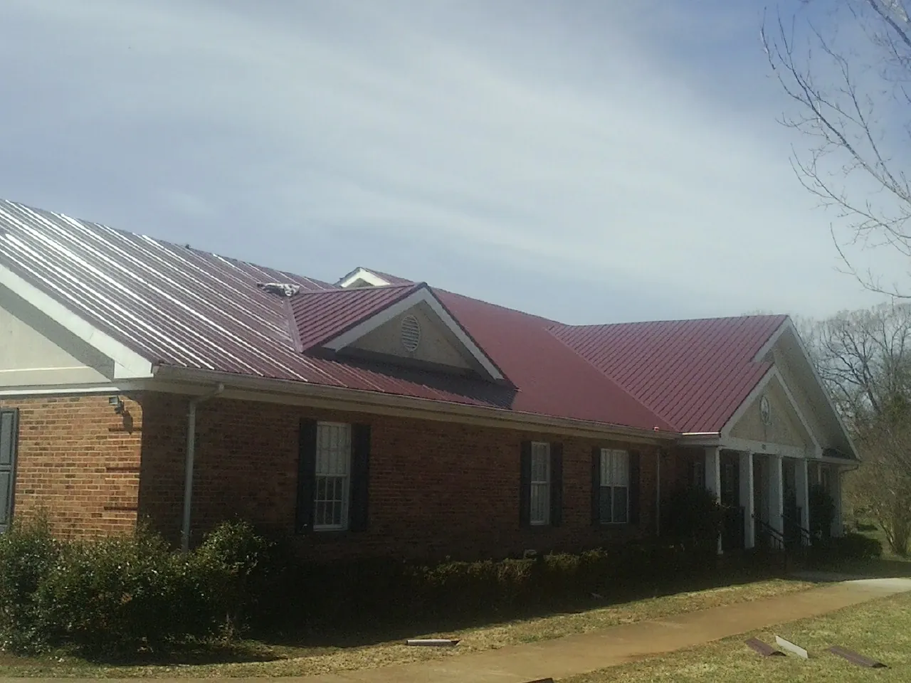 Red metal roof with gabled entries on a long brick building, from a Hail Damage Roof Repair job in Mineral Springs