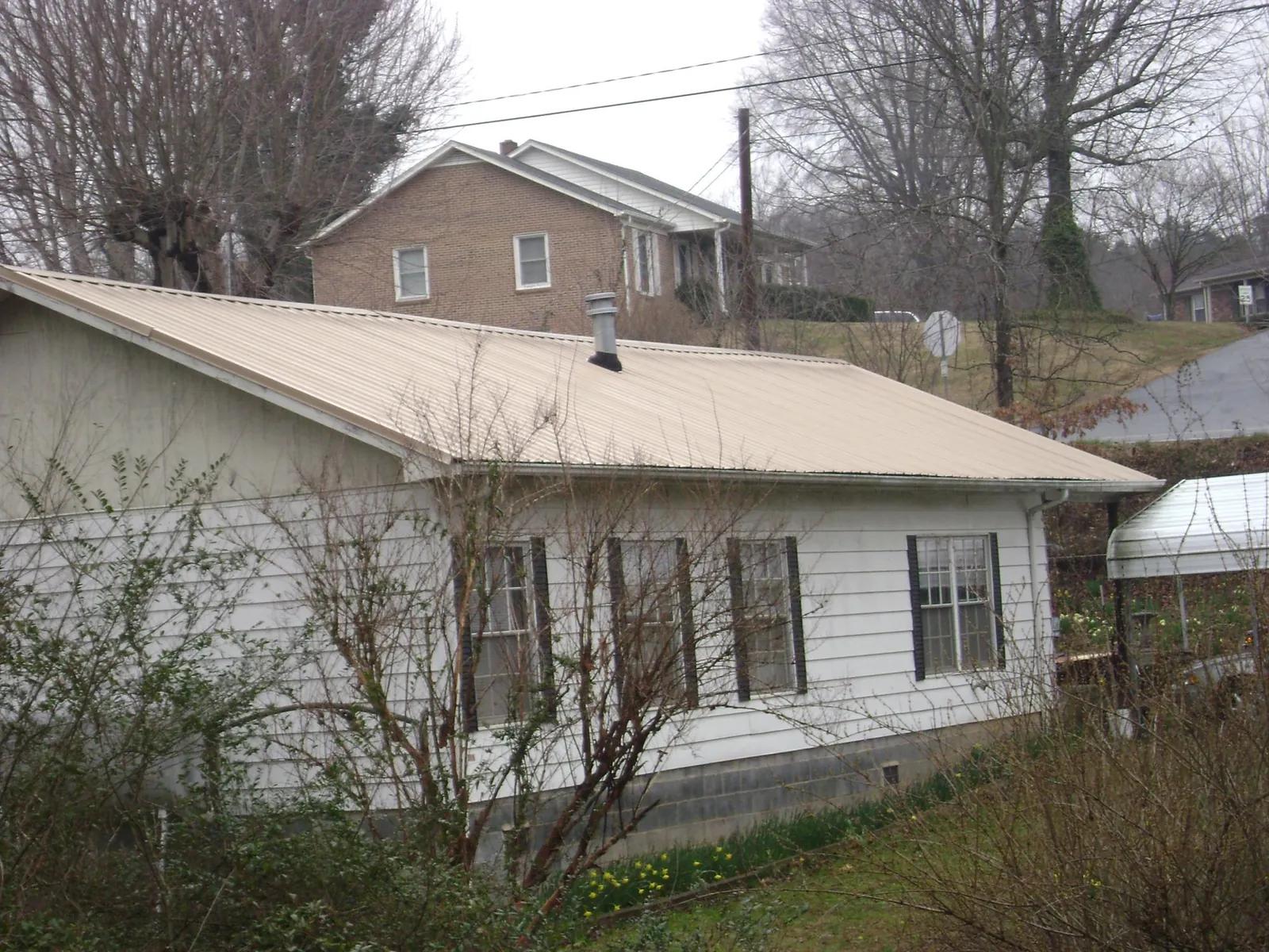 Tan metal roof on a white sided house set into a hillside — Commercial Roofing by Roofing Brothers in Mineral Springs